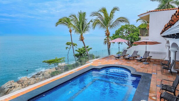A swimming pool with a view of the sea, surrounded by lounge chairs and umbrellas.