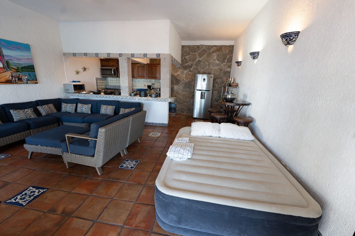Un espacio habitable compacto con sofá, cama, zona de cocina y pared de piedra.