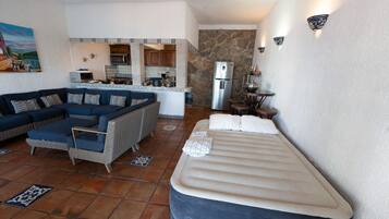 Un espacio habitable compacto con sofá, cama, zona de cocina y pared de piedra.