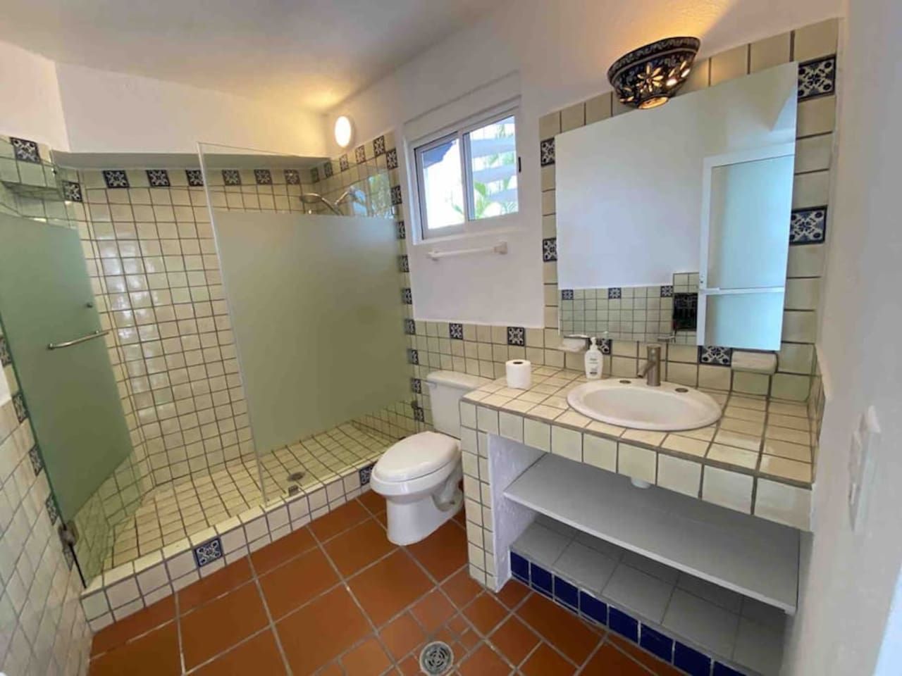 A bathroom with a shower, toilet, sink, and a window.