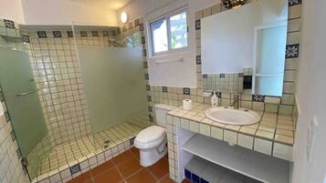 A bathroom with a shower, toilet, sink, and a window.
