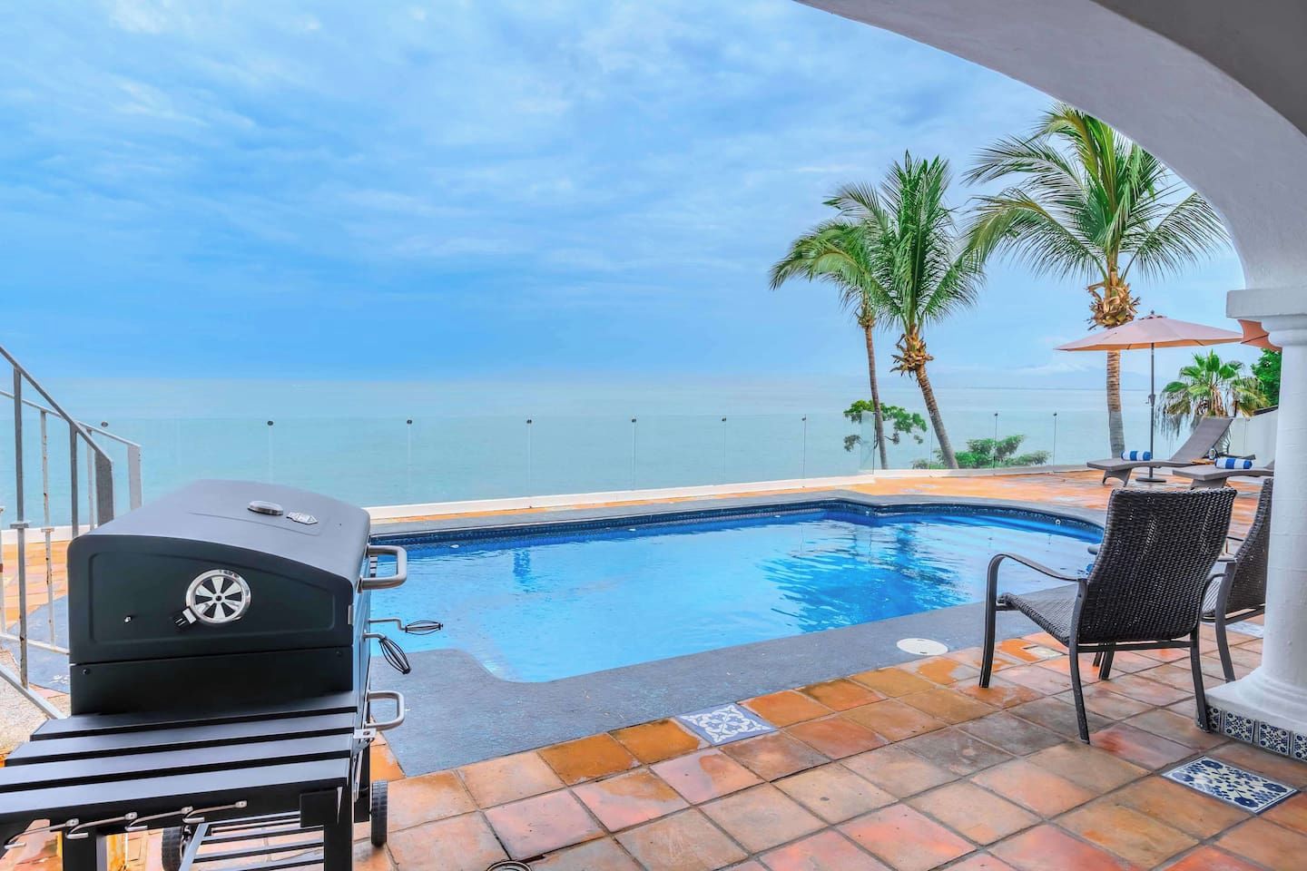 Una piscina con vistas al océano, una parrilla y sillas de descanso.