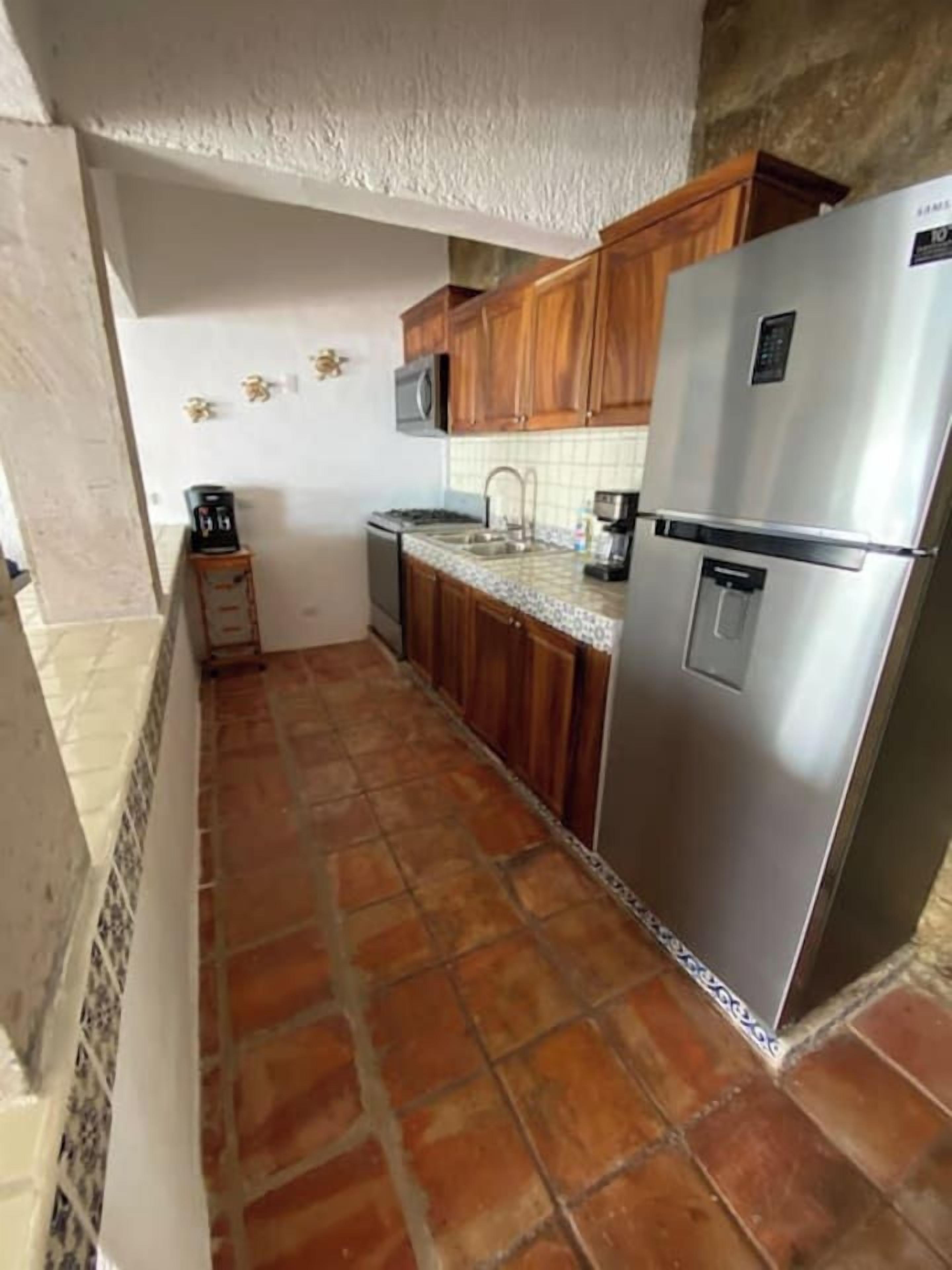 A compact kitchen with a refrigerator, microwave, and wooden cabinets.