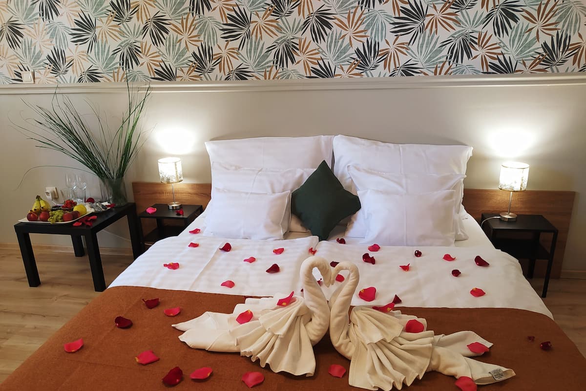 A hotel room with a neatly made bed, rose petals, and a swan-shaped towel arrangement.