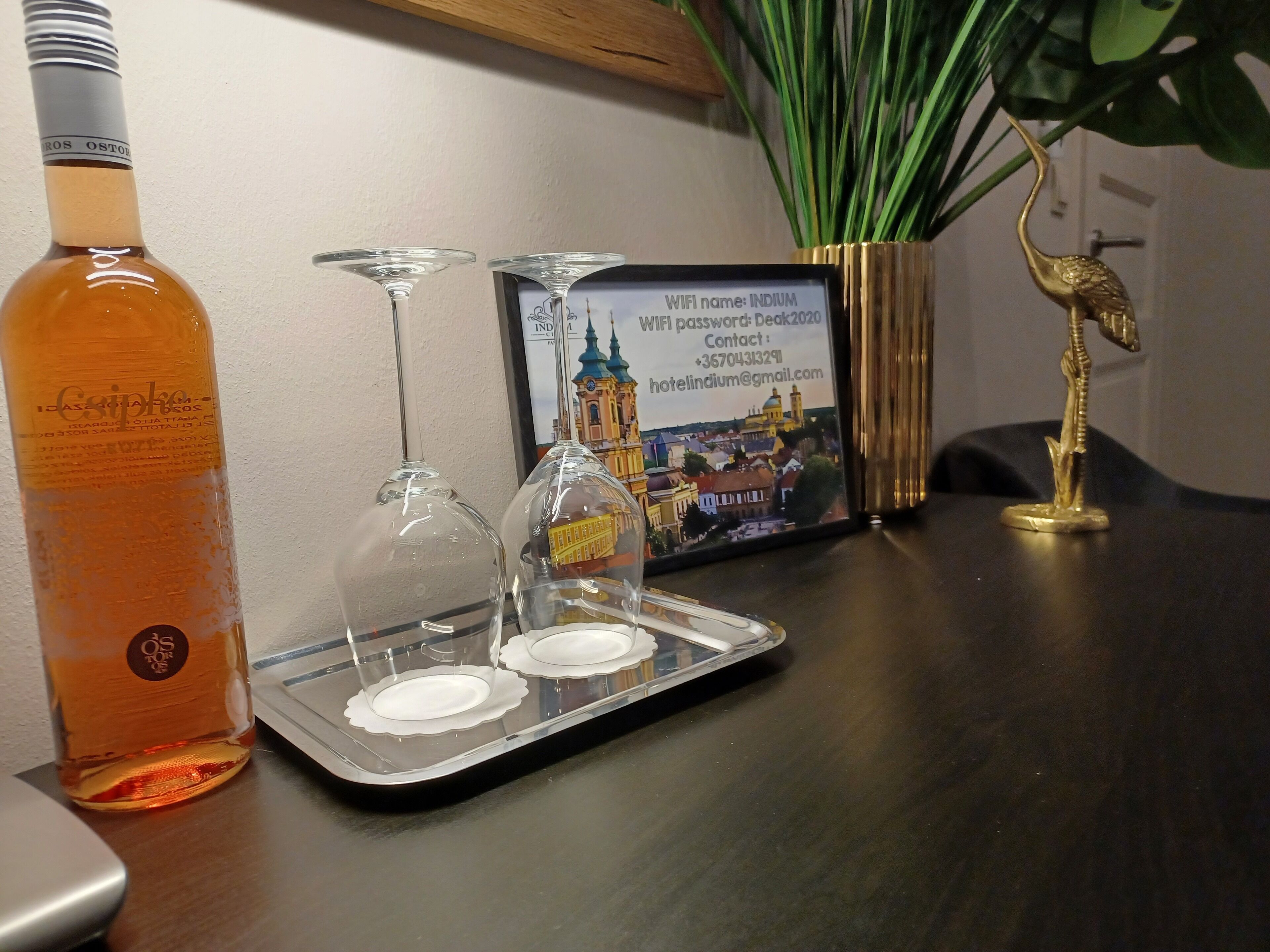Eine Flasche Crespicco, zwei Weingläser, ein Tablett mit einem Bilderrahmen und eine goldene Statue auf einem Tisch.