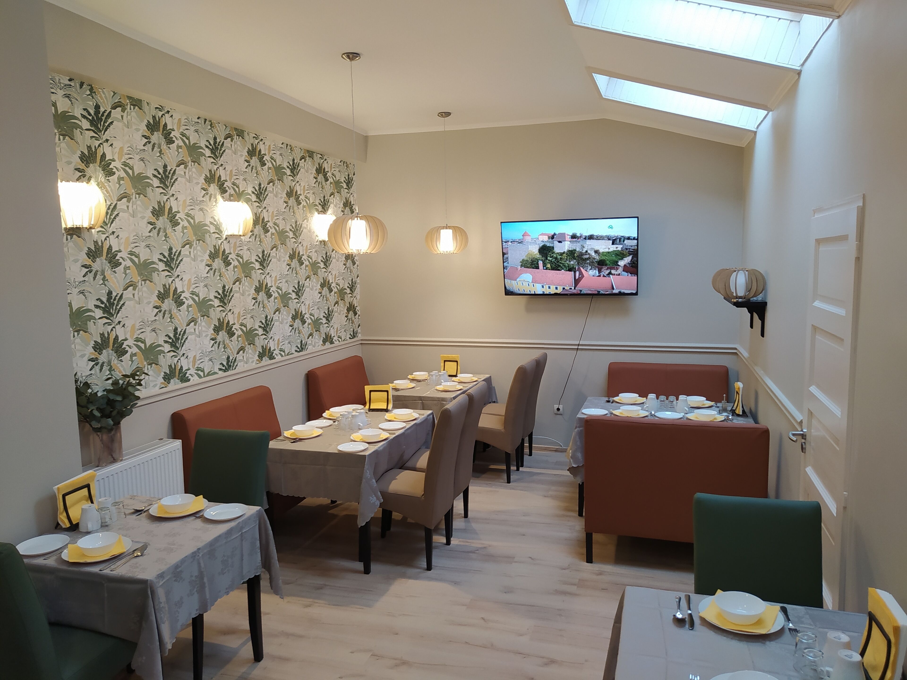 Een eethoek met tafels voor vier personen, een aan de muur bevestigde televisie en uitzicht op gebouwen door het dakraam.