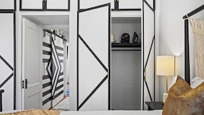 Un dormitorio con cama, mesita de noche, lámpara y armario con puerta a rayas.