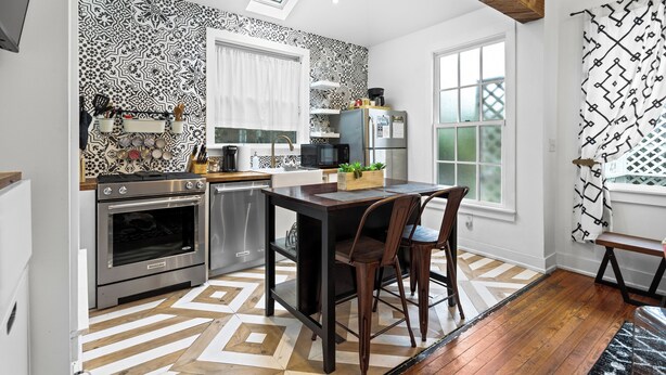 Una cocina moderna con papel tapiz estampado, tragaluz, piso de madera y un comedor con dos sillas.