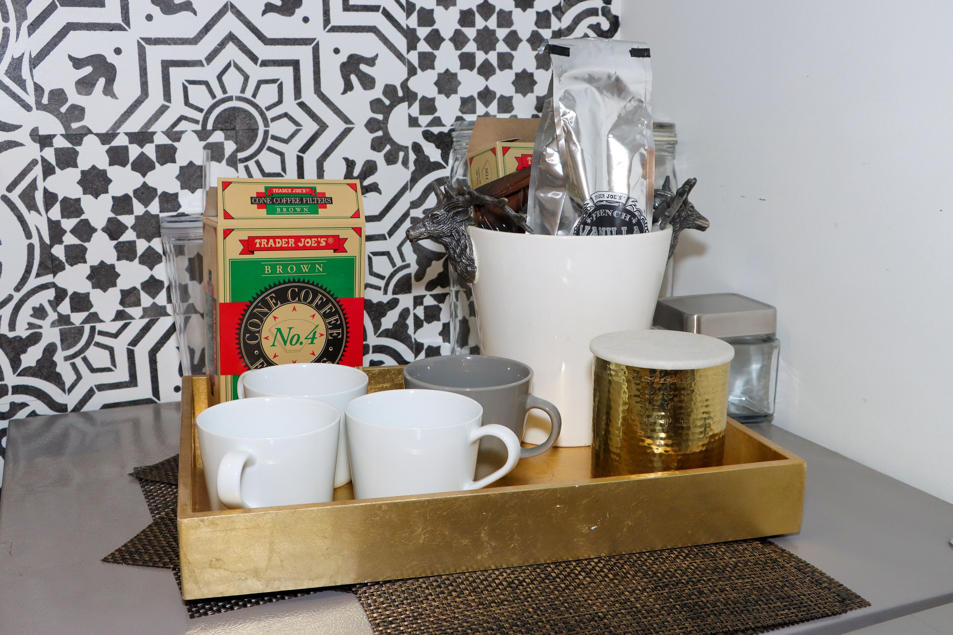 A tray with coffee mugs, a box of coffee filters, a coffee grinder, and a decorative container.
