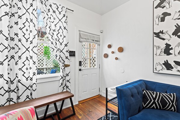 A room with a wooden bench, a blue sofa, a patterned wall hanging, and a door with a geometric window view.