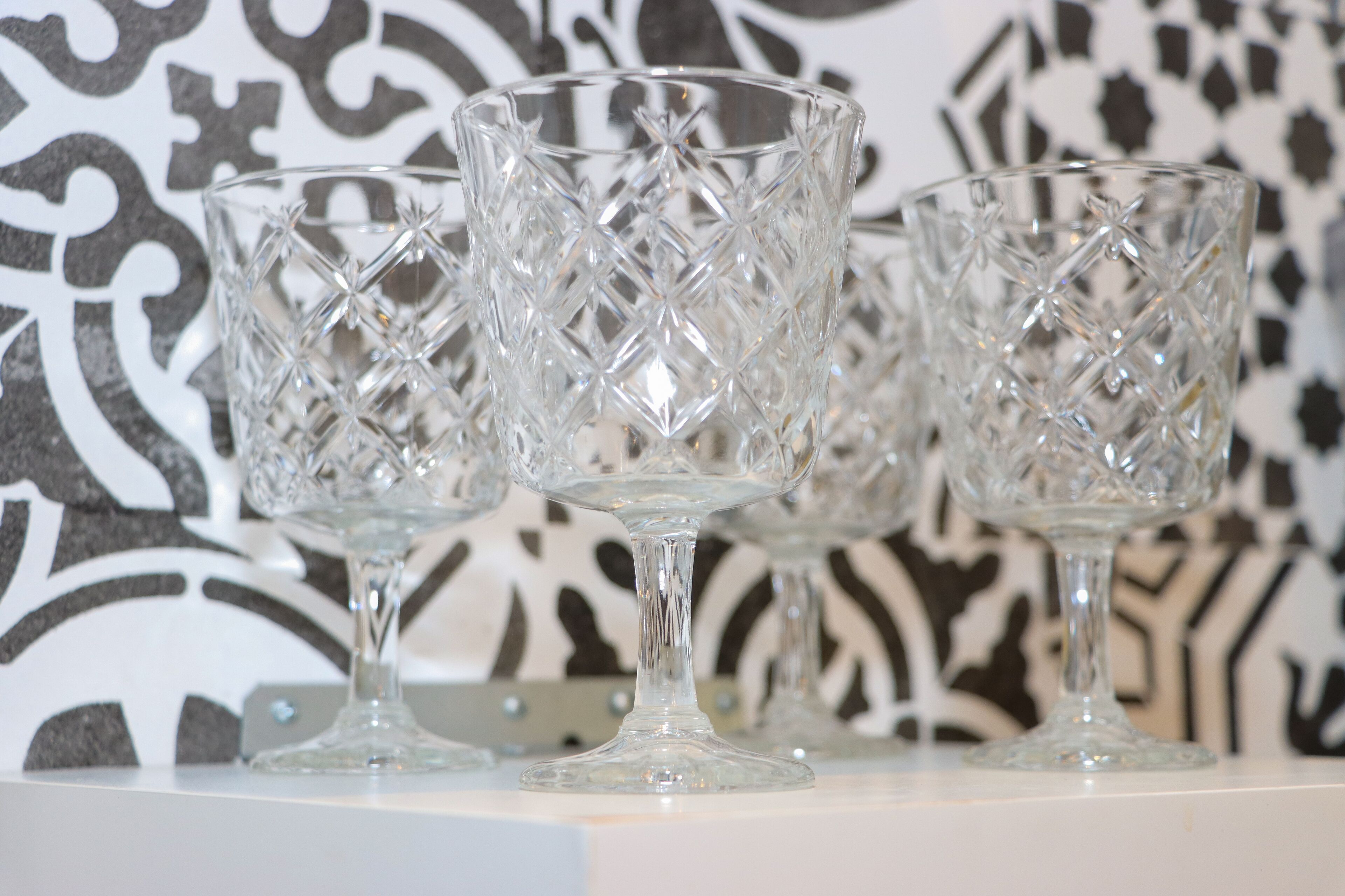 Three clear glass goblets with a diamond pattern on a white surface against a black and white patterned background.