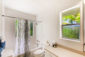Un baño con bañera, inodoro y ventana con vistas a la vegetación.