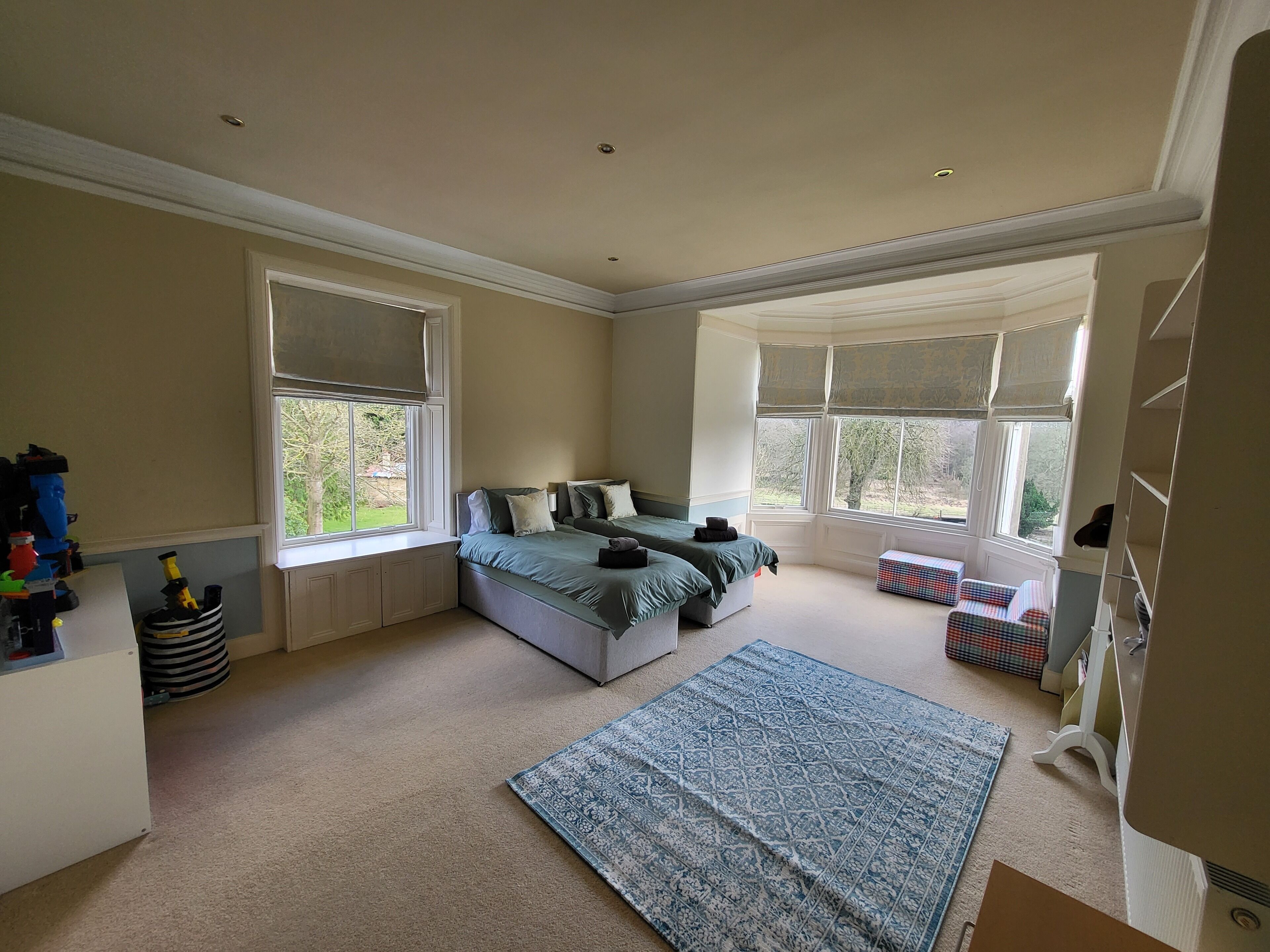 Een slaapkamer met een groot raam, een bed, een bankje en een vloerkleed.