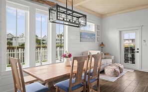 A dining area with a wooden table and chairs, a hanging light fixture, and a view of the outside. - Casa Driftwood, Pool, Dock & Beach Boardwalk (Port Aransas)
