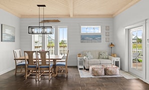 A dining area with a wooden table and chairs, a sofa with patterned cushions, and a view of the outside. - Casa Driftwood, Pool, Dock & Beach Boardwalk (Port Aransas)