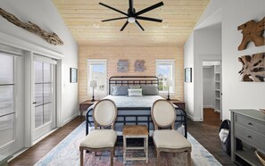 A bedroom with a bed, two chairs, a small table, a ceiling fan, and wooden walls. - Casa Driftwood, Pool, Dock & Beach Boardwalk (Port Aransas)