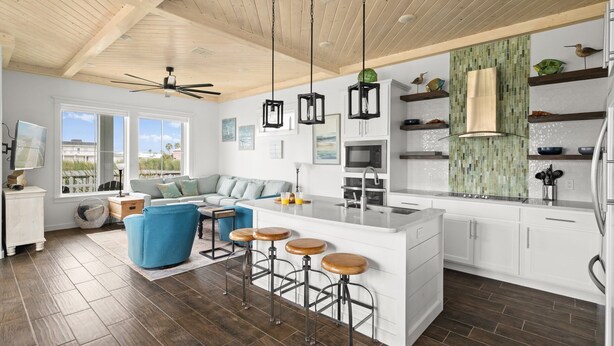 Una cocina moderna con una isla central, taburetes de bar y un comedor con sofá.