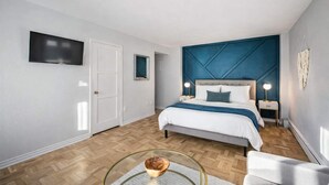 Quarto moderno com uma cama grande, uma televisão de tela plana na parede e uma mesinha com uma tigela.