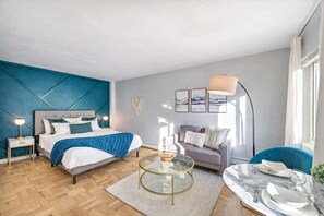 A modern bedroom with a bed, bedside tables, a sofa, a coffee table, and a dining area with a table set for two.