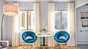 Uma sala de jantar moderna com duas cadeiras azuis, uma mesa redonda e uma luminária pendente.
