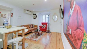 A living room with a wooden floor, a red armchair, a white sofa, a coffee table, and a painting on the wall.