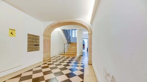 A hallway with a checkered floor, an arched doorway, and a staircase leading to another room.