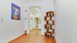 Un couloir doté d’un plancher en bois, d’un extincteur, d’un tableau représentant un lama et d’une étagère en bois ornée d’objets décoratifs.