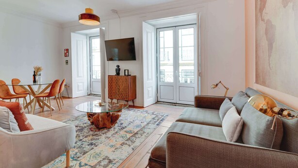 Un salon moderne avec une table basse en verre, un canapé, une table à manger avec des chaises et un téléviseur fixé au mur.