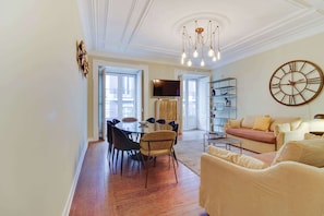 A spacious living area with a dining table, chairs, a sofa, and a large wall clock. - Chiado | 4 Bedrooms + 2 Baths | Parking (Lisboa)