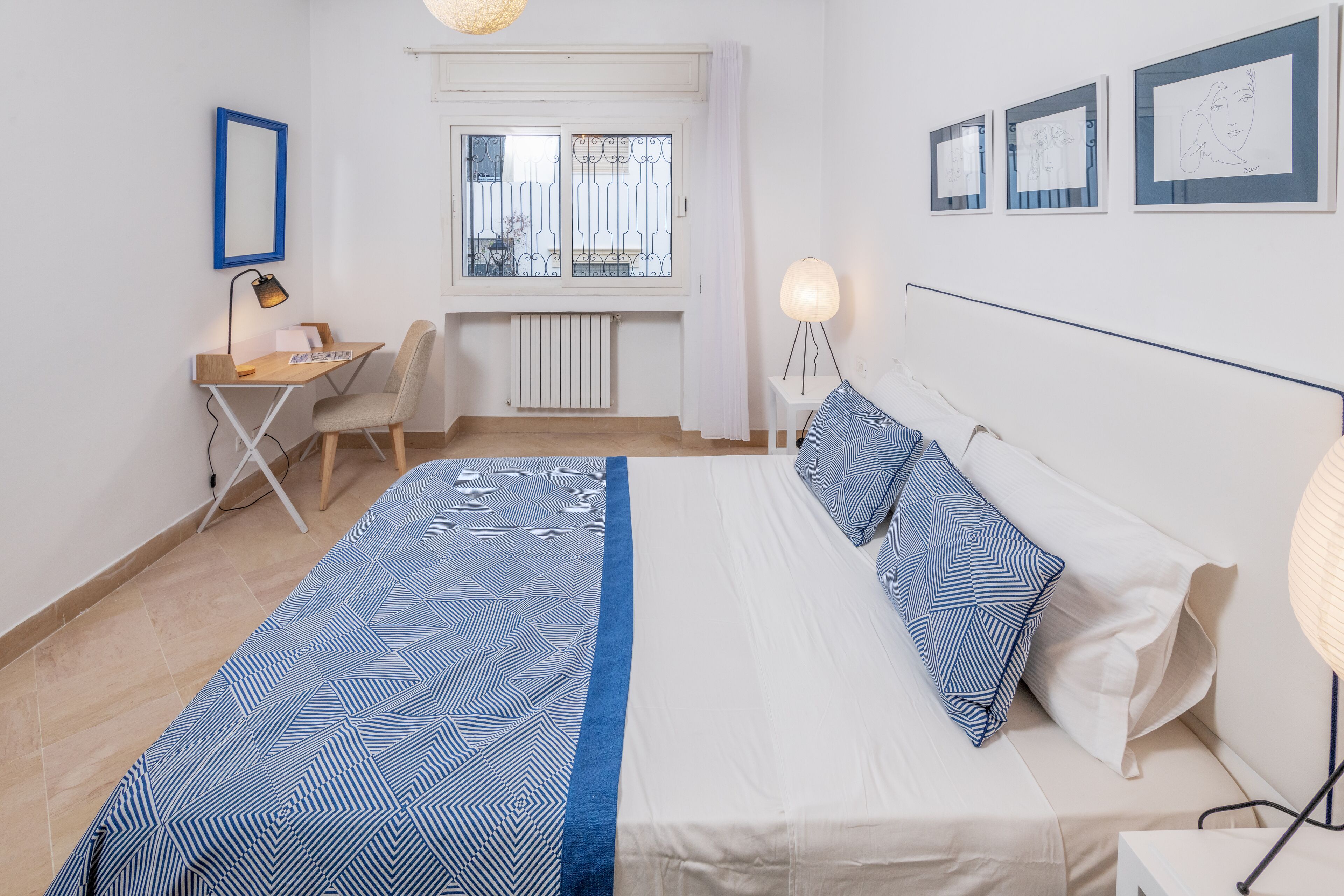 A bedroom with a bed, a desk, a chair, and a window with a view.