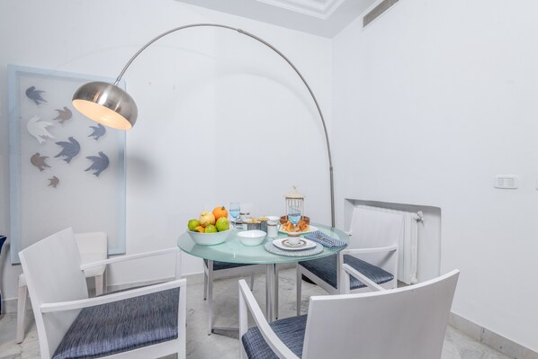 Un comedor con una mesa redonda de vidrio, sillas blancas con cojines azules, una lámpara de metal y una pared con siluetas de tiburones.