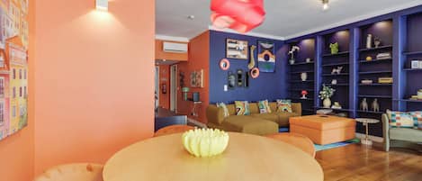 A modern living room with a round wooden table, a sofa, and a bookshelf.