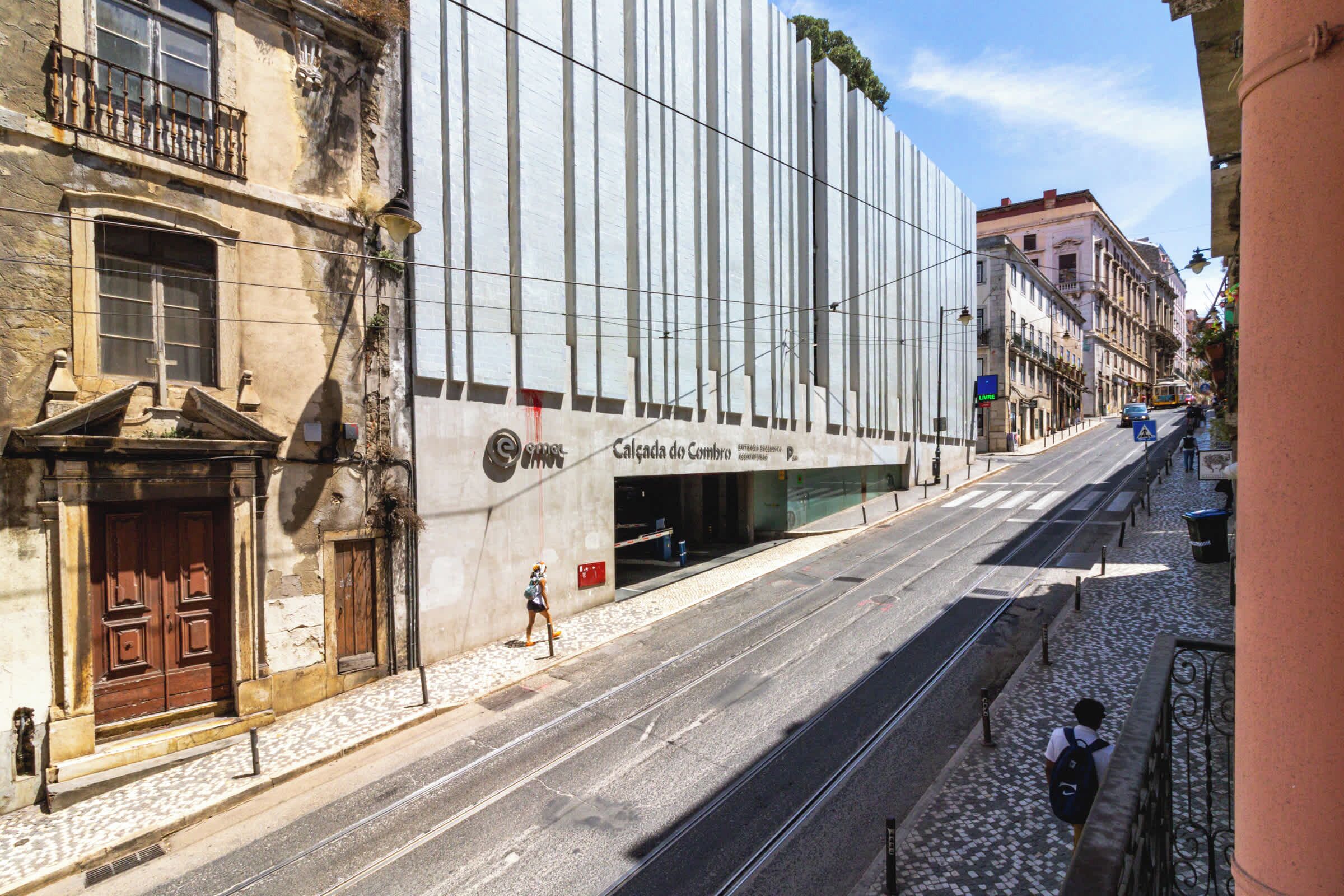 A street with a tram line, a building with a modern facade, and a pedestrian crossing.