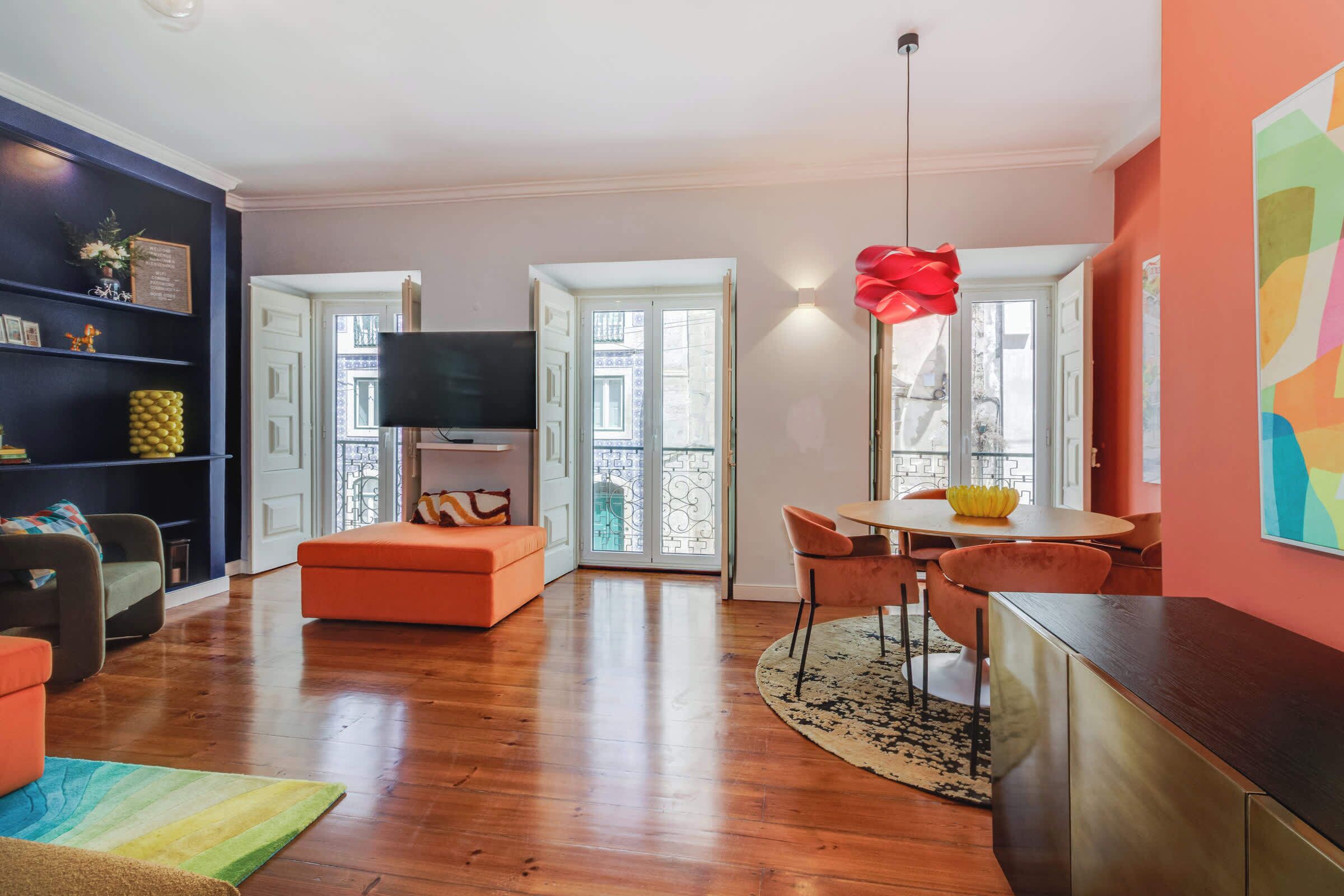 A modern living room with a flat-screen TV, a dining area with a round table, and a large red pendant light.