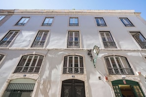 A multi-story building with a series of windows and balconies, a central entrance with a door, and a green awning over the entrance. - Bairro Alto | 4 Bedrooms + 4 Baths | Sleeps 8 (Lisboa)