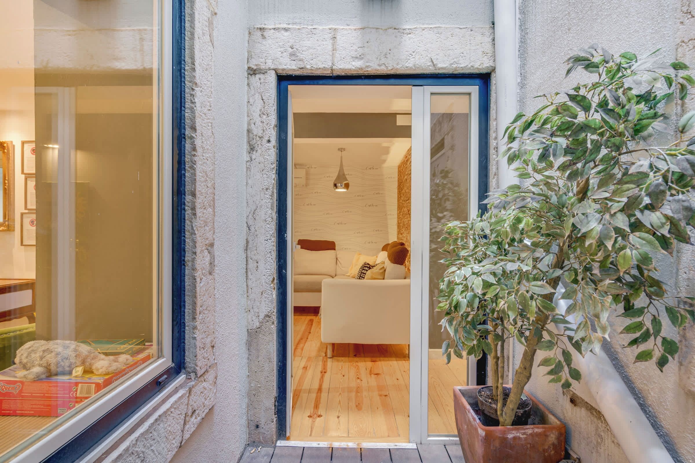 A narrow entrance with a glass door leading to a living room with a sofa and a hanging light fixture.