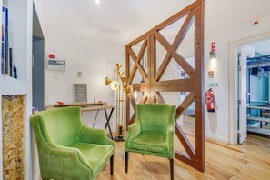 Ein Zimmer mit zwei grünen Polstersesseln, einer Holzvertäfelung, einem Schreibtisch mit Lampe und einem Feuerlöscher.