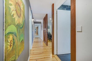Passadís amb sòl de fusta, una porta blanca i un mur amb un quadre de girasol.
