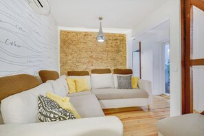Ein modernes Wohnzimmer mit einer Eckcouch, einer Ziegelwand als Blickfang und einer Pendelleuchte.