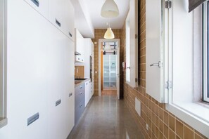 A narrow hallway with a kitchen area on the left, a door with a frosted glass panel, and a window on the right. - Chiado | Triplex 6 Bedrooms | Terrace + Parking (Lisboa)