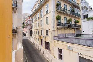 A narrow street flanked by multi-story buildings with balconies, a paved road, and a yellow building on the left.