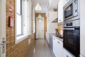 Una cocina estrecha con microondas, horno y una lámpara colgante.