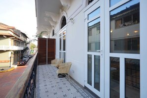 A balcony with wicker chairs, a tiled floor, and a view of the street.