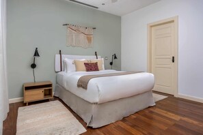 Ein Schlafzimmer mit einem Bett, Nachttischlampen, einem Nachttisch, einem Wandbehang aus Makramee und einer Tür.