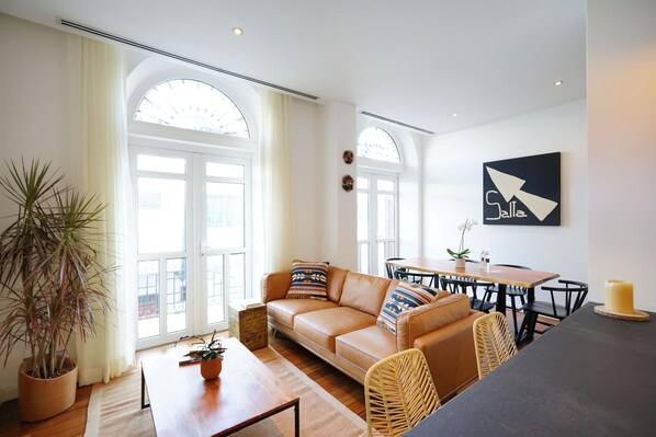 A modern living room with a leather sofa, a dining table, and a large window.