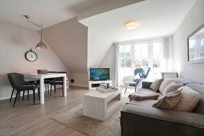 Una sala de estar moderna con una mesa de centro blanca, un sofá, un televisor y un comedor con sillas y una mesa.