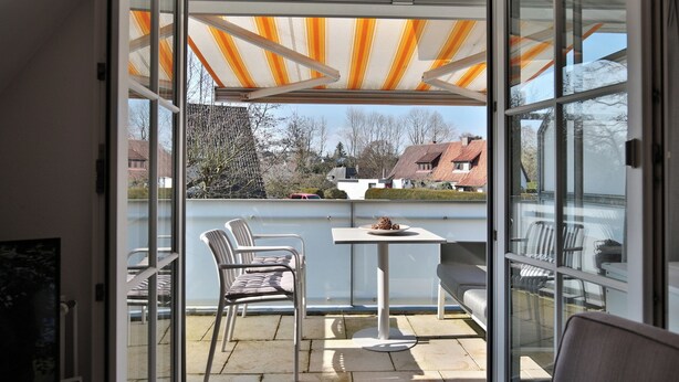 A balcony with a glass door, a table, chairs, and a striped awning. - Domizil Gartenstraße 4 Appartement 7 Treibgut (Timmendorfer Strand)