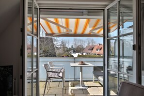 A balcony with a glass door, a table, chairs, and a striped awning. - Domizil Gartenstraße 4 Appartement 7 Treibgut (Timmendorfer Strand)