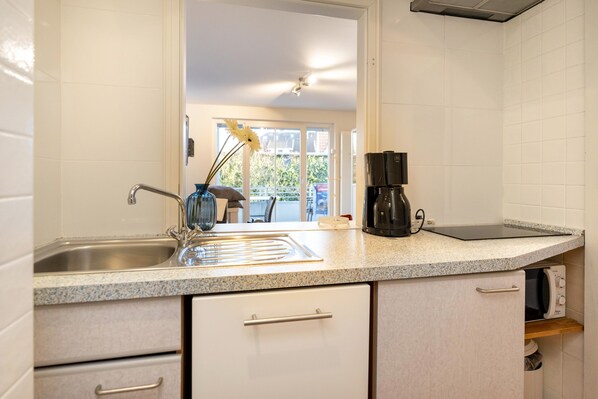 A modern kitchen with white cabinets, a granite countertop, a coffee maker, and a view of the outdoors. - Bergstraße 62 Vacation Home, Heimathafen Apartment (Timmendorfer Strand)