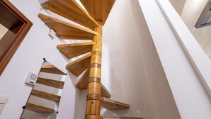 Una escalera de caracol con escalones de madera y un pilar central, que lleva a una plataforma con un rascador para gatos y una pared blanca.